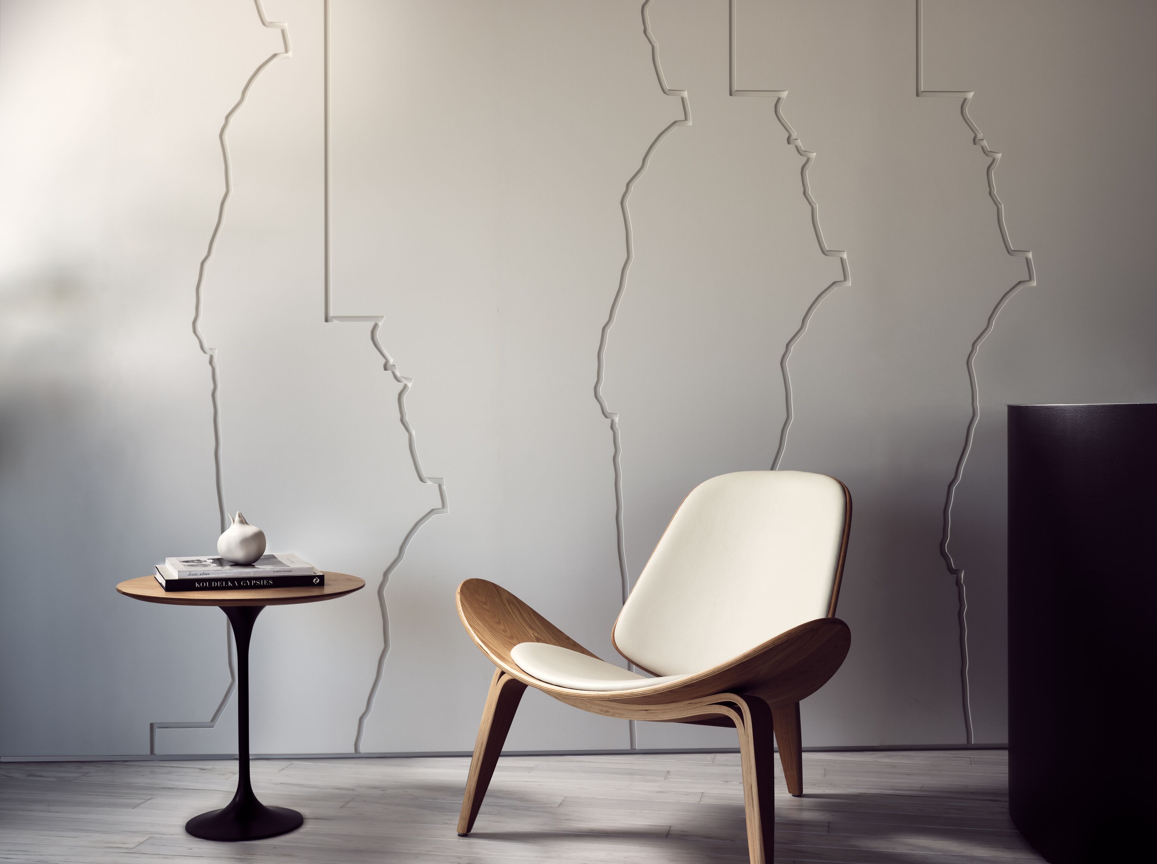 Una habitación moderna con un diseño minimalista, que incluye una silla de madera, una mesita redonda con un libro y una pared con arte abstracto de líneas.