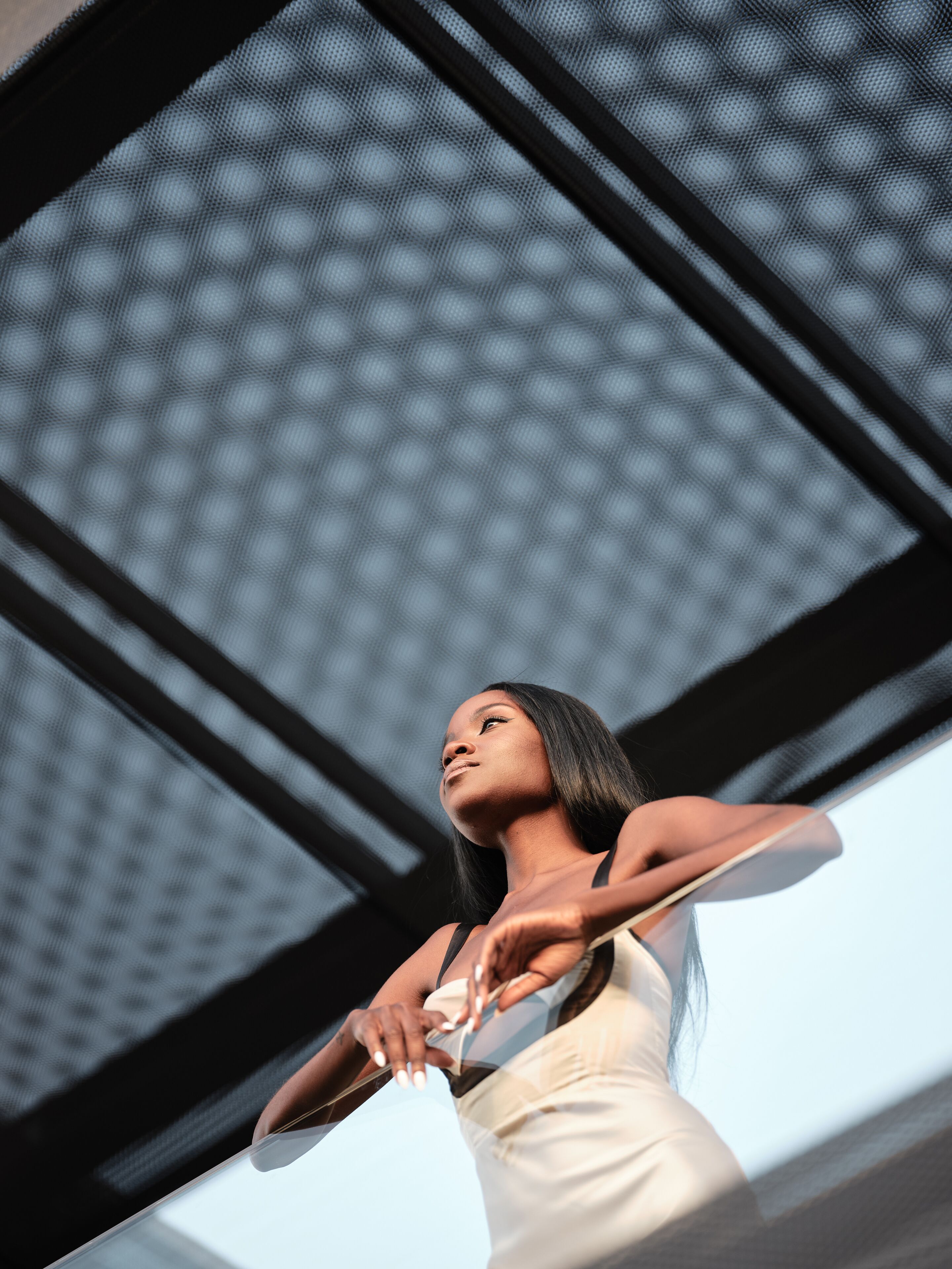 A person holding a pair of scissors, standing in front of a building with a mesh facade.