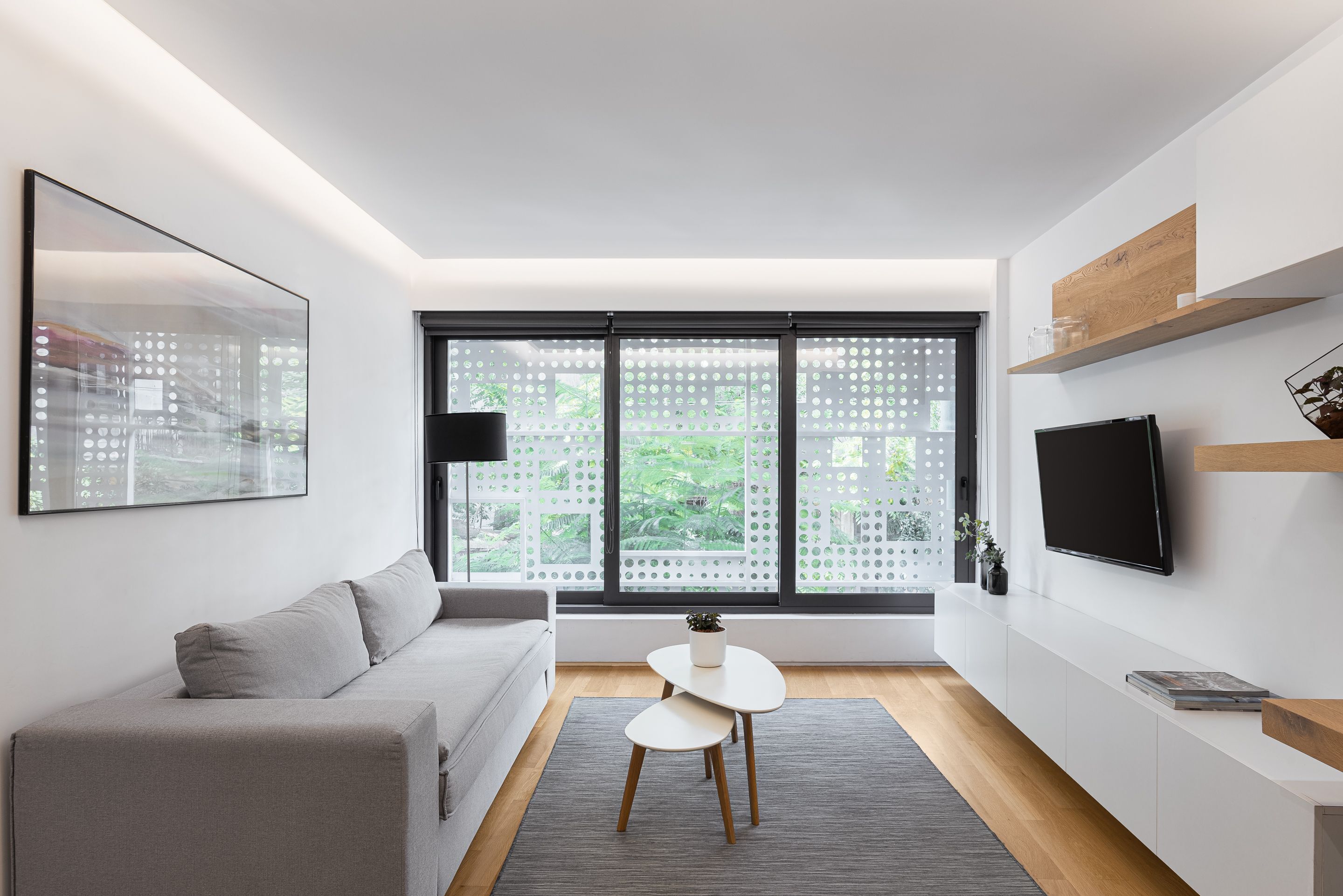 A modern living room with a grey sofa, a small white table, and a TV mounted on the wall.
