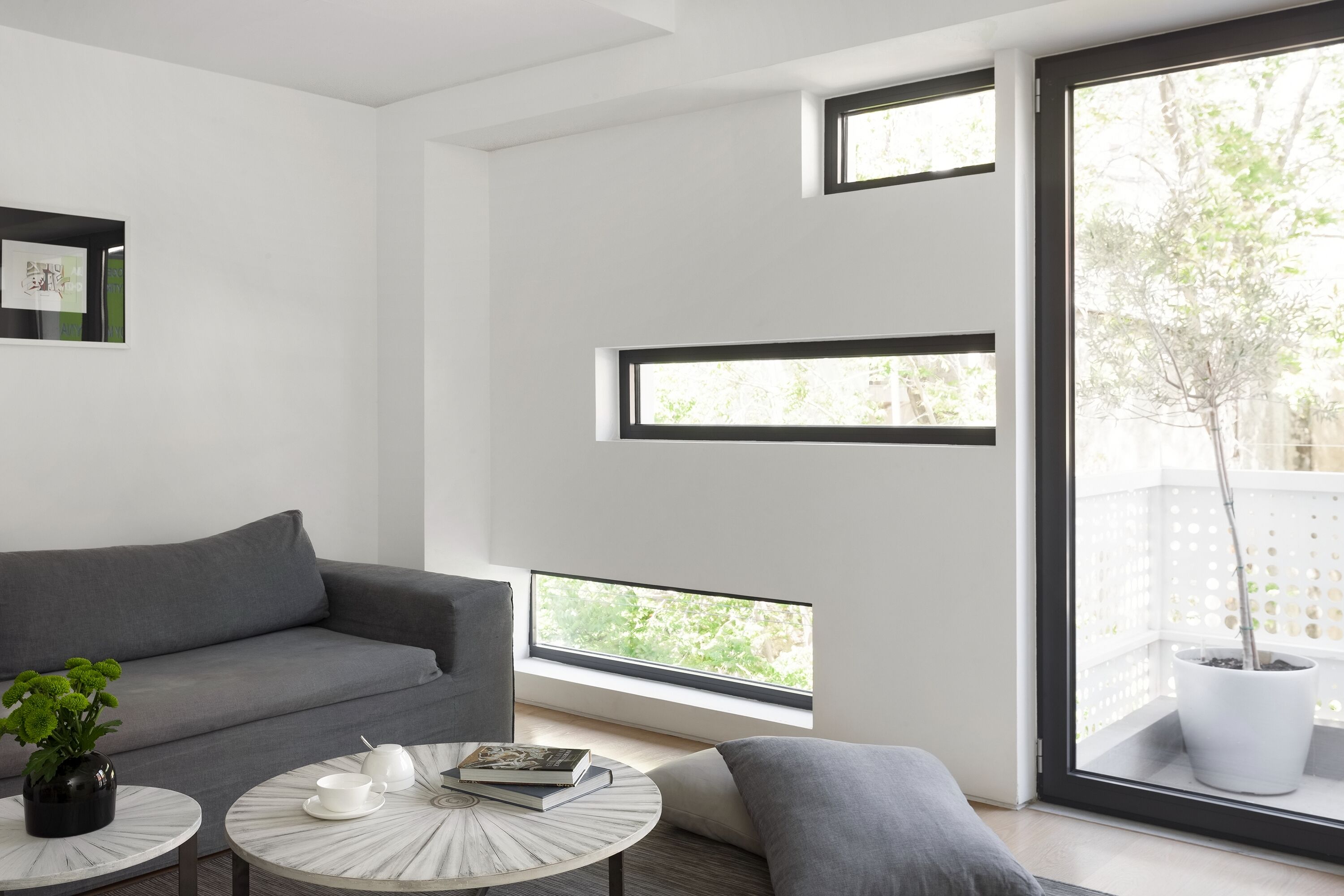 A modern living room with a grey sofa, a round coffee table with decorative items, and a large window with a view of greenery.