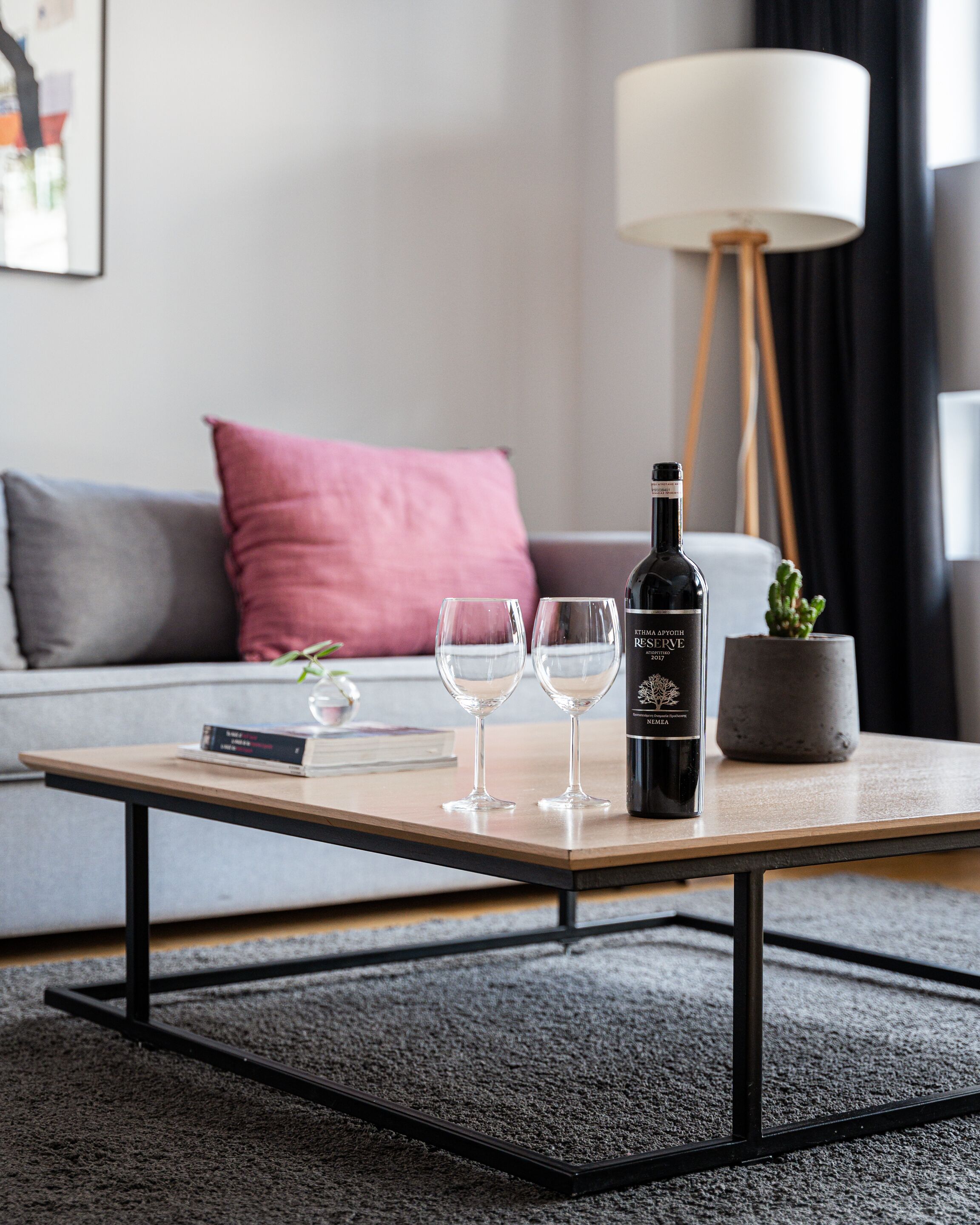 Ein modernes Wohnzimmer mit einer Couch, einem Couchtisch, zwei Weingläsern, einer Weinflasche und einer Stehlampe.