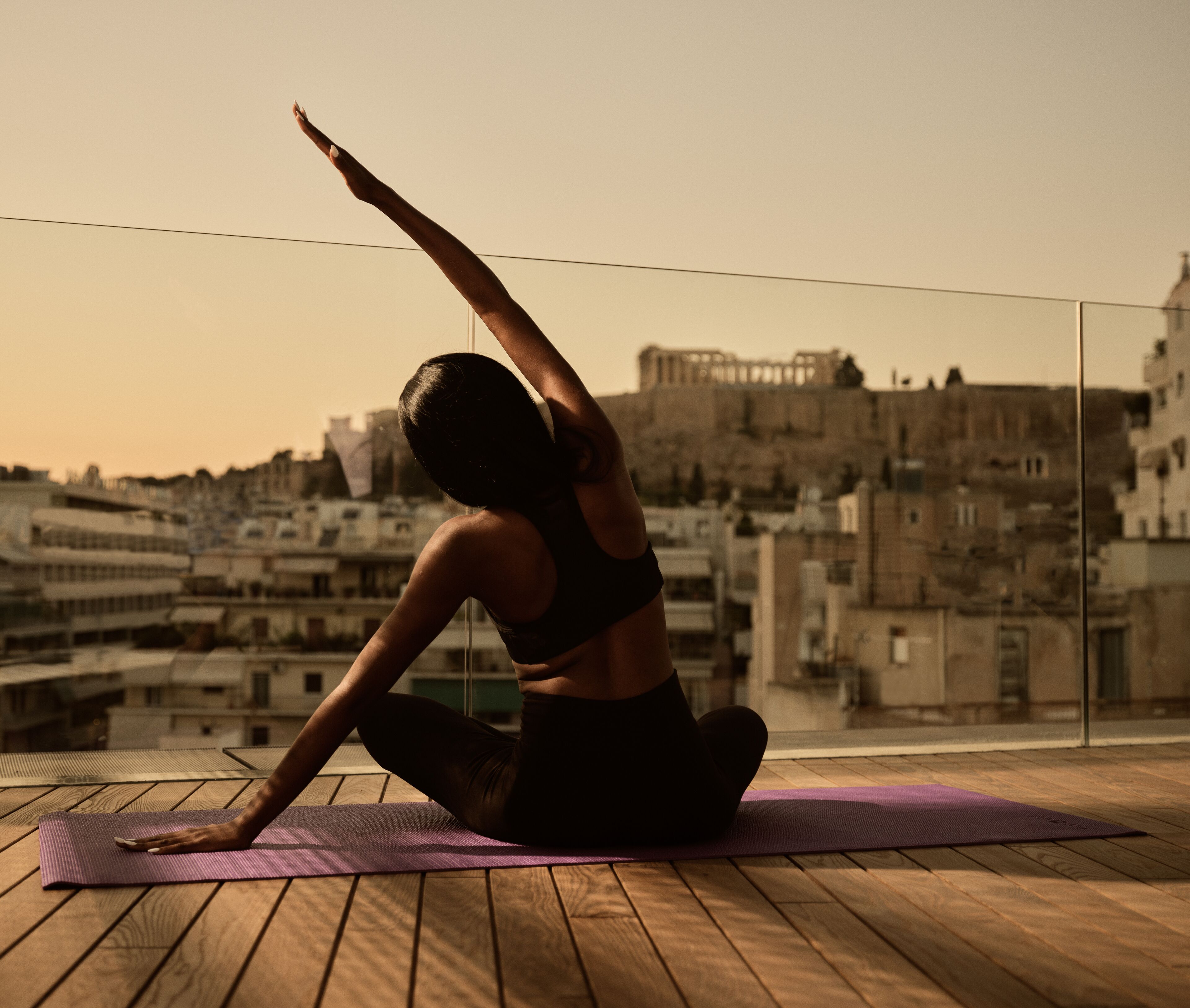 A person performing yoga on a wooden deck with a cityscape in the background.