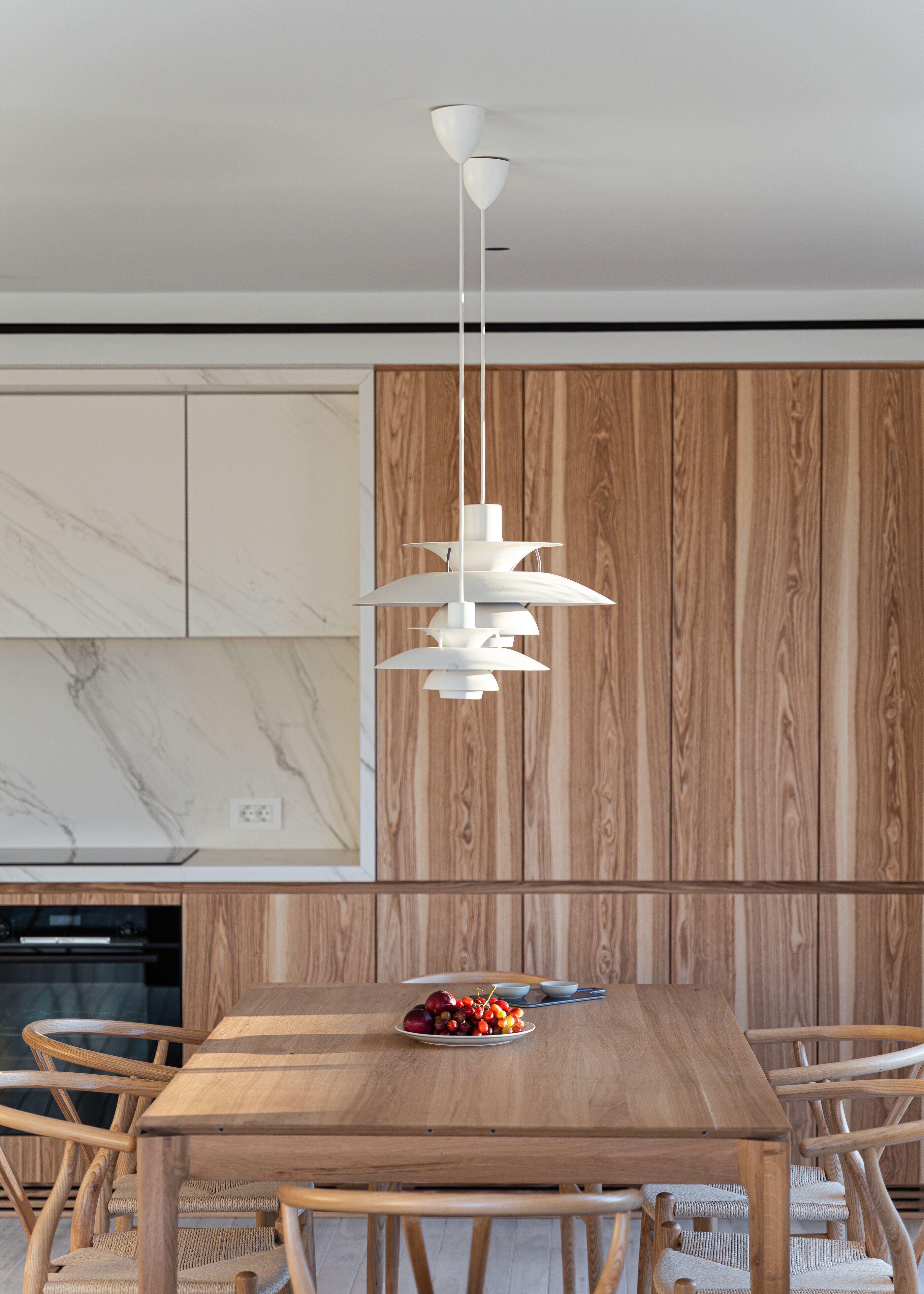 A modern dining area with a wooden table, wicker chairs, and a white pendant light.