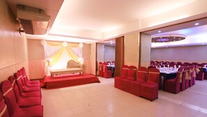 A banquet hall with rows of red chairs, a stage with a red carpet, and a large table set for a banquet. - Britannia Hotel (Sylhet)