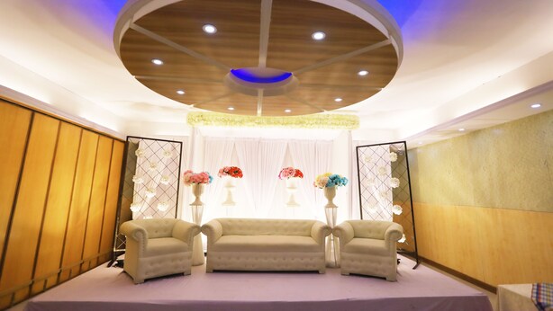 A room with a stage, two armchairs, and floral arrangements. - Britannia Hotel (Sylhet)