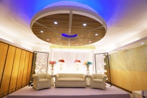 A room with a stage, two armchairs, and floral arrangements. - Britannia Hotel (Sylhet)