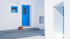 Ein weißes Gebäude mit blauer Tür und Fenster, ein kleiner Topfpflanze und ein grauer Markise.