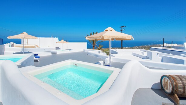 Ein Poolbereich auf dem Dach mit blauem Himmel, weißer Architektur und Blick aufs Meer.