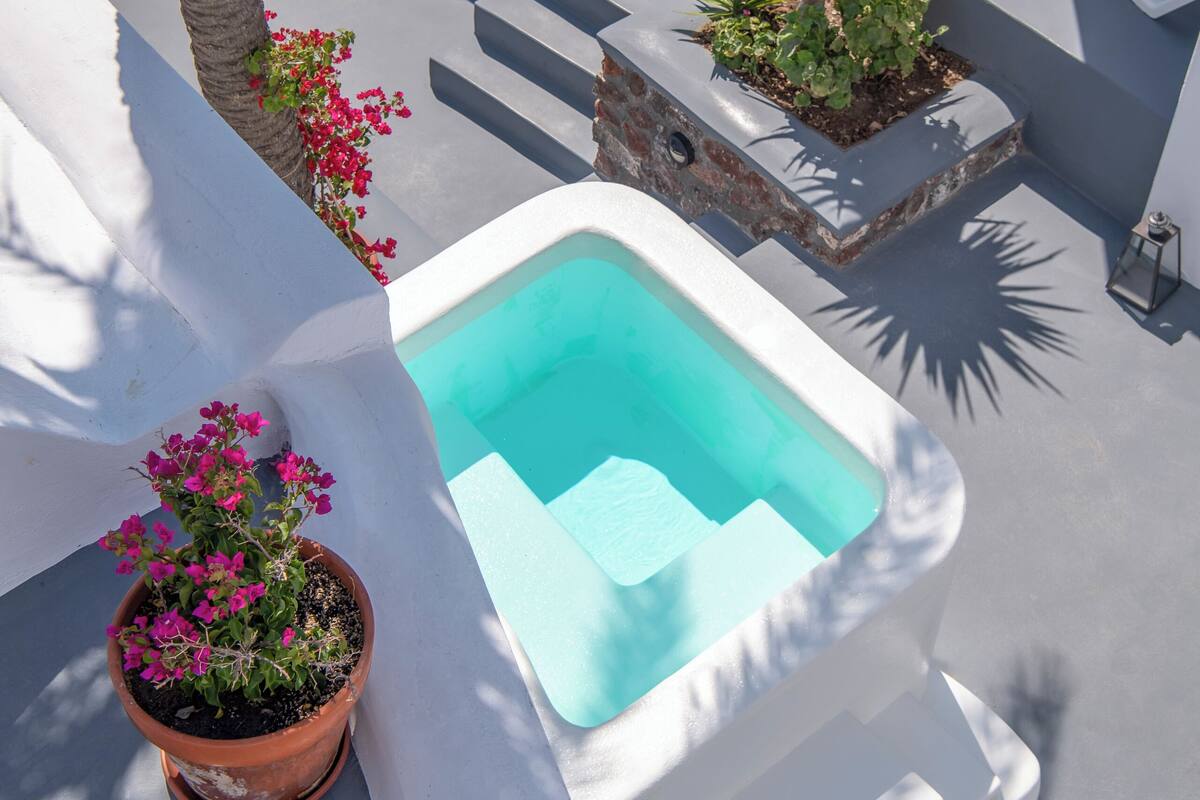 A rooftop pool area with a small pool, white lounge chairs, and a bar area.