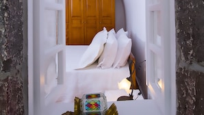 Ein schmales, abgeschlossenes Zimmer mit einem Bett, einem Holzschrank und einem kleinen Tisch mit Dekoration.
