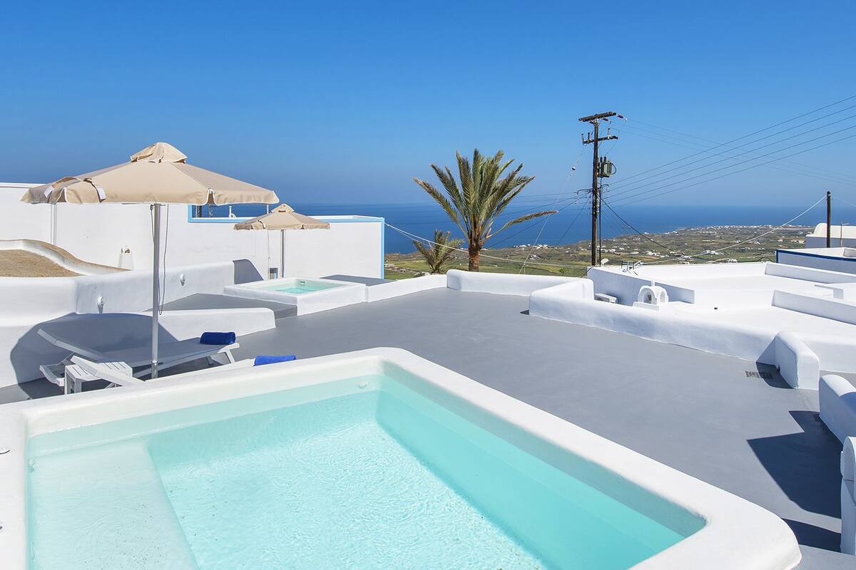 A rooftop pool with clear blue water, surrounded by white structures and a view of the sea.