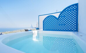 A modern infinity pool with a clear view of the ocean, a blue lattice gate, and a small flag. - Kadia Traditional Residences (Santorini)