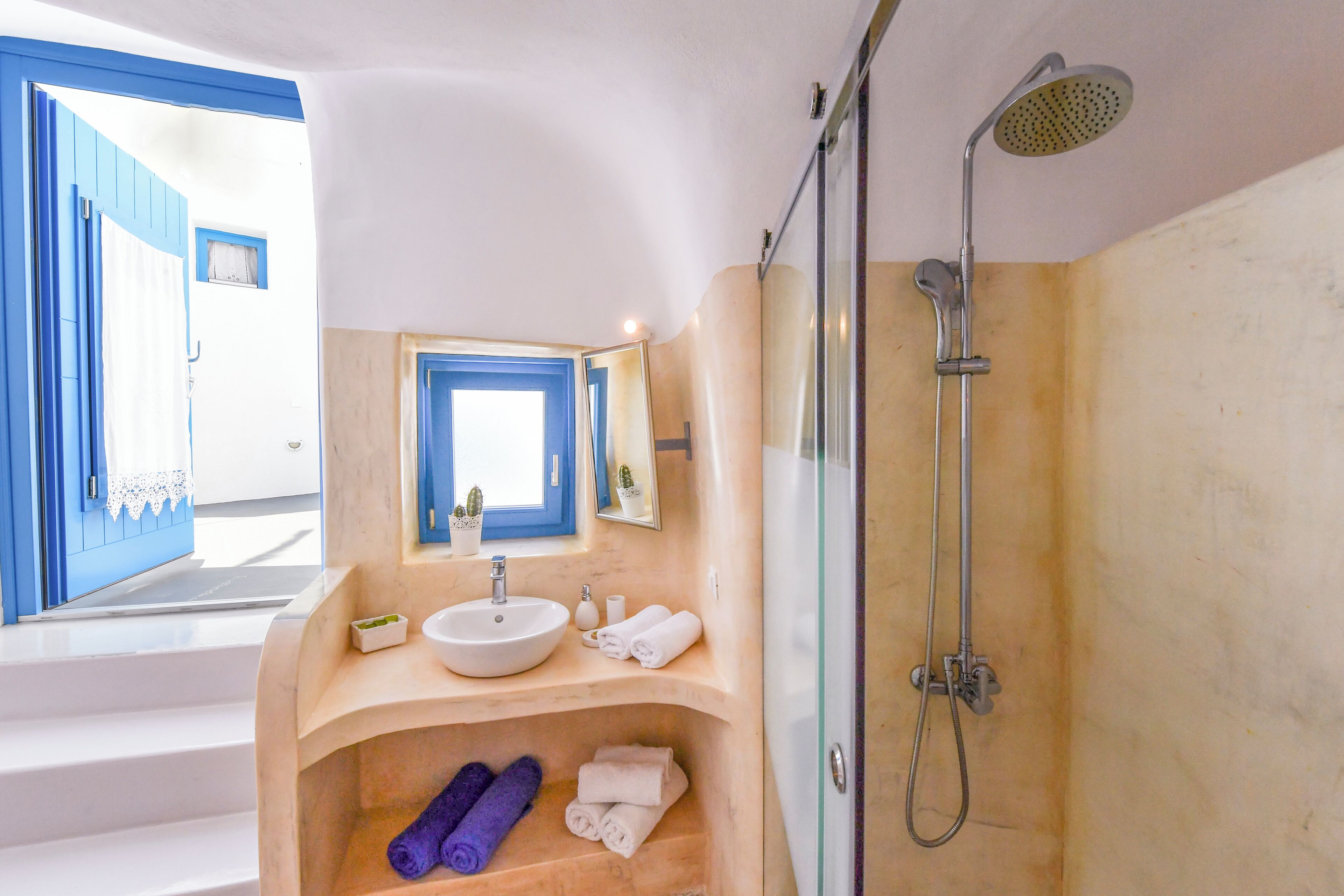 Une salle de bain avec un lavabo blanc, un miroir, une douche et une fenêtre.