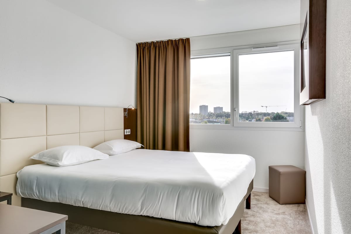 Une chambre d’hôtel avec un lit, une table de chevet, une fenêtre avec des rideaux et une vue sur le paysage urbain.