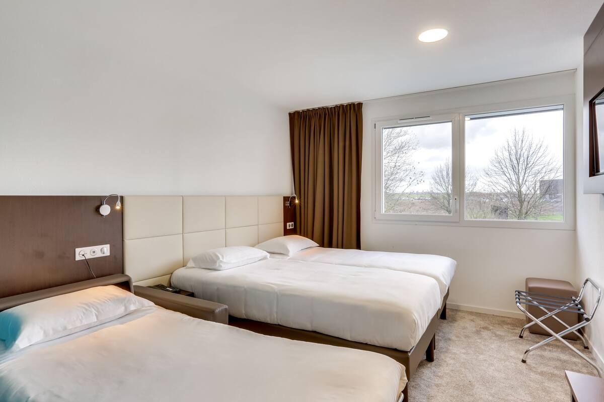 Une chambre d’hôtel avec deux lits, une fenêtre avec des rideaux, une table de chevet et une chaise.
