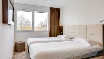 Een hotelkamer met twee bedden, een raam met gordijnen, een nachtkastje en een klein krukje.