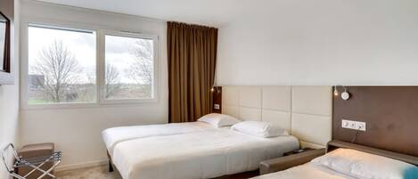 Une chambre d’hôtel avec deux lits, une fenêtre avec des rideaux, une table de chevet et une lampe fixée au mur.