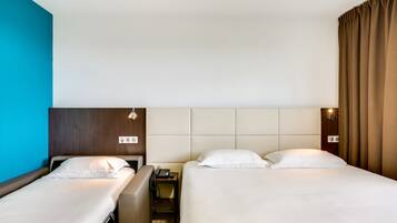 A hotel room with two beds, a bedside table with a phone, and a wall-mounted light fixture.