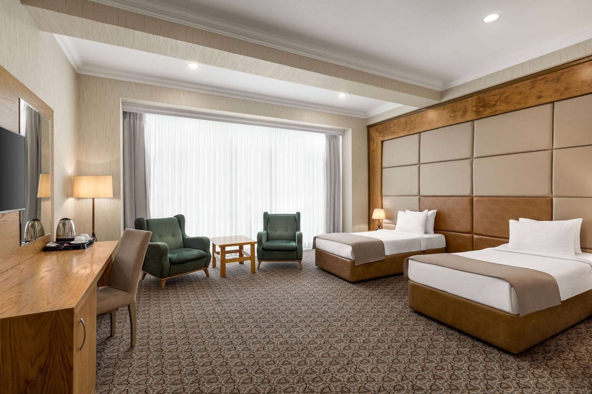 A hotel room with a large bed, two smaller beds, a desk, two chairs, a TV, and a large window with curtains.