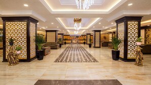 Um hall amplo com carpete quadriculado, pilares decorativos e um lustre.