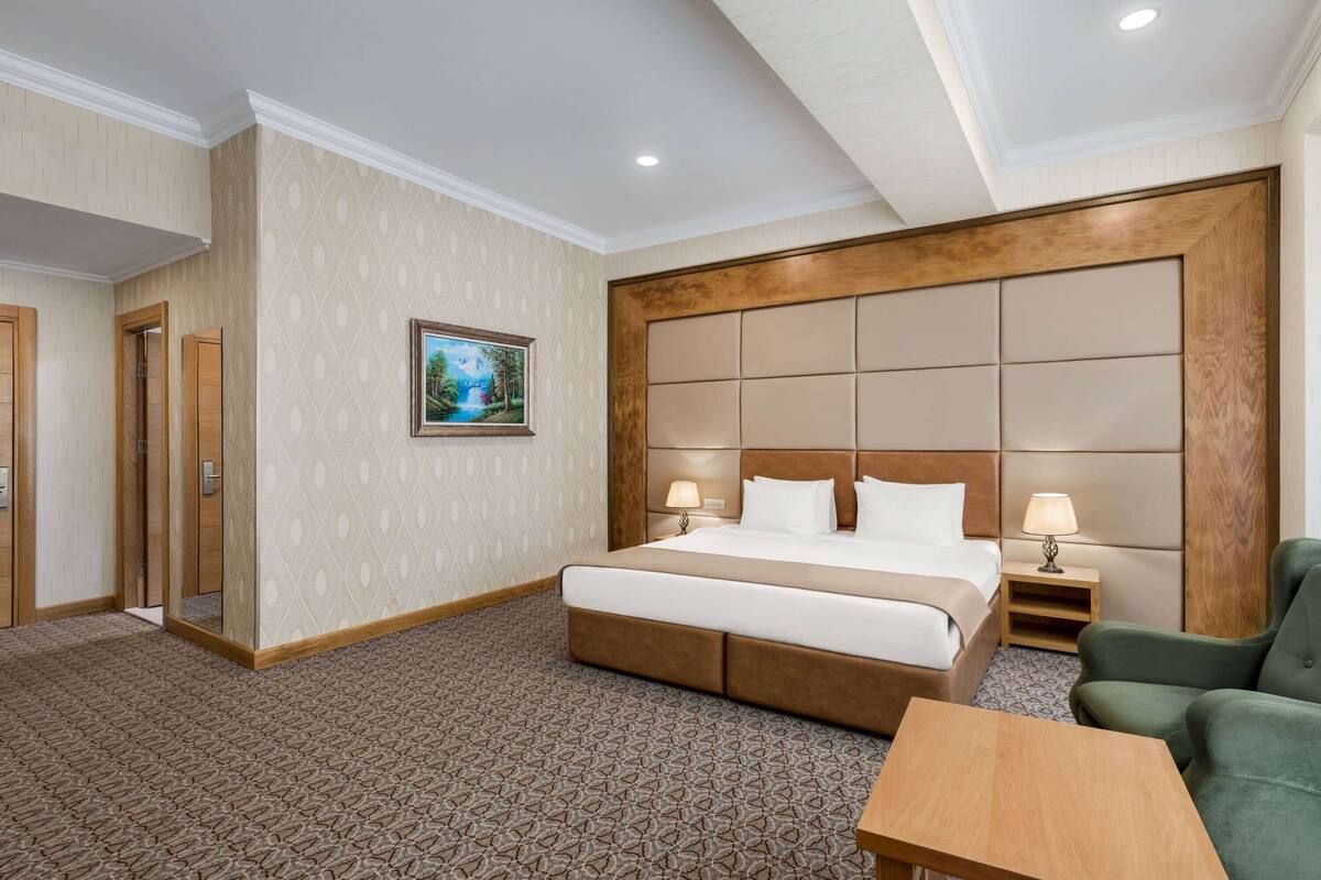 A hotel room with a large bed, two bedside tables, a green armchair, and a carpeted floor.