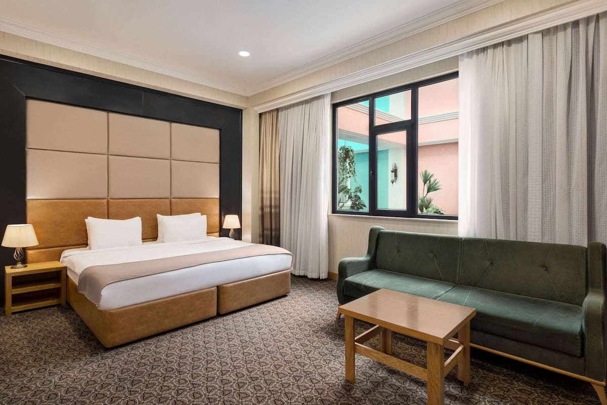 A hotel room with a large bed, a green sofa, a wooden table, and a window with curtains.