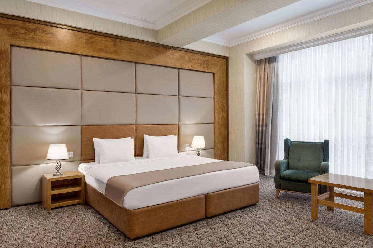 A hotel room with a large bed, two bedside tables with lamps, a green armchair, and a small table.