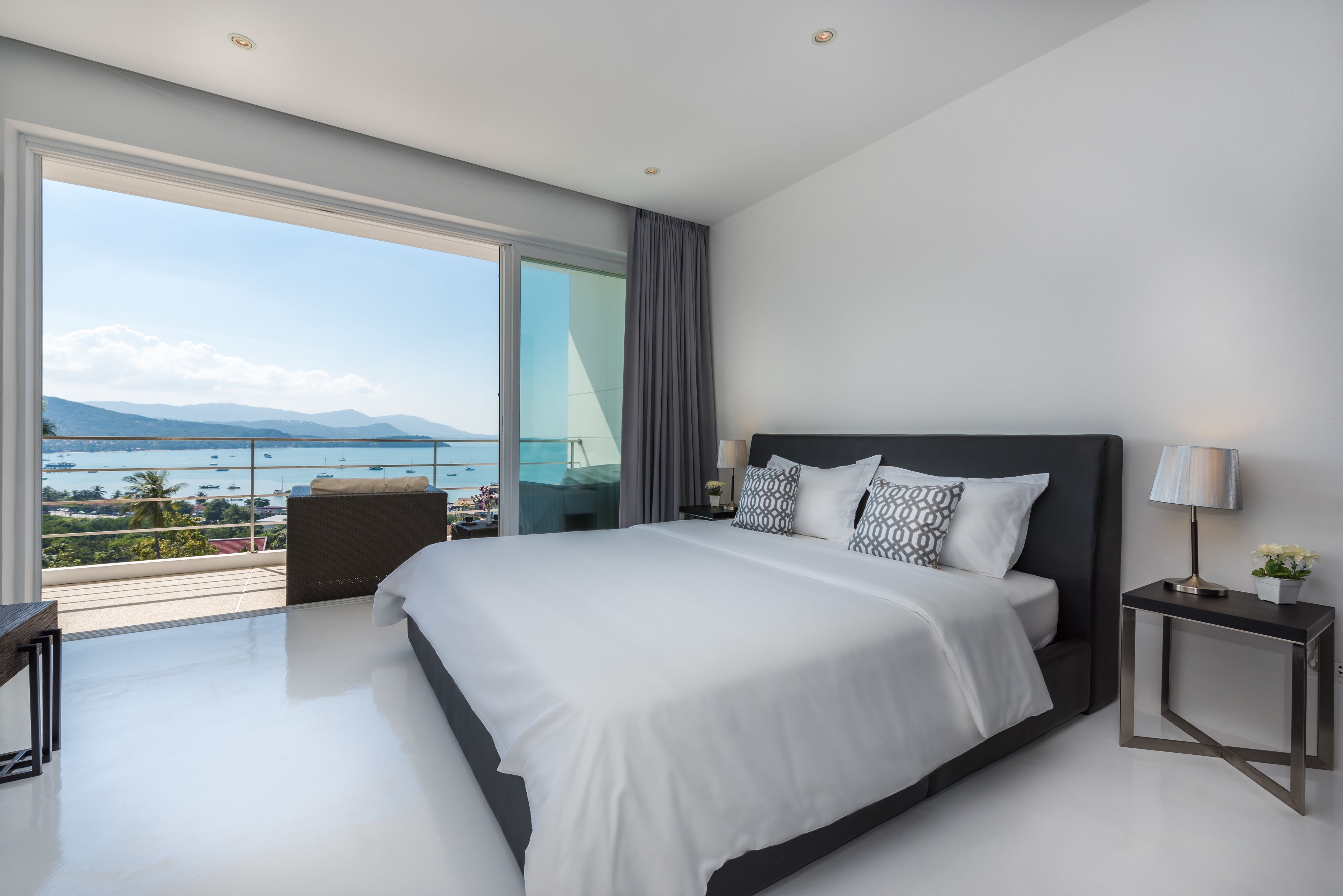 Una habitación de hotel moderna con una cama grande, una mesita de noche, vistas al mar y un balcón.