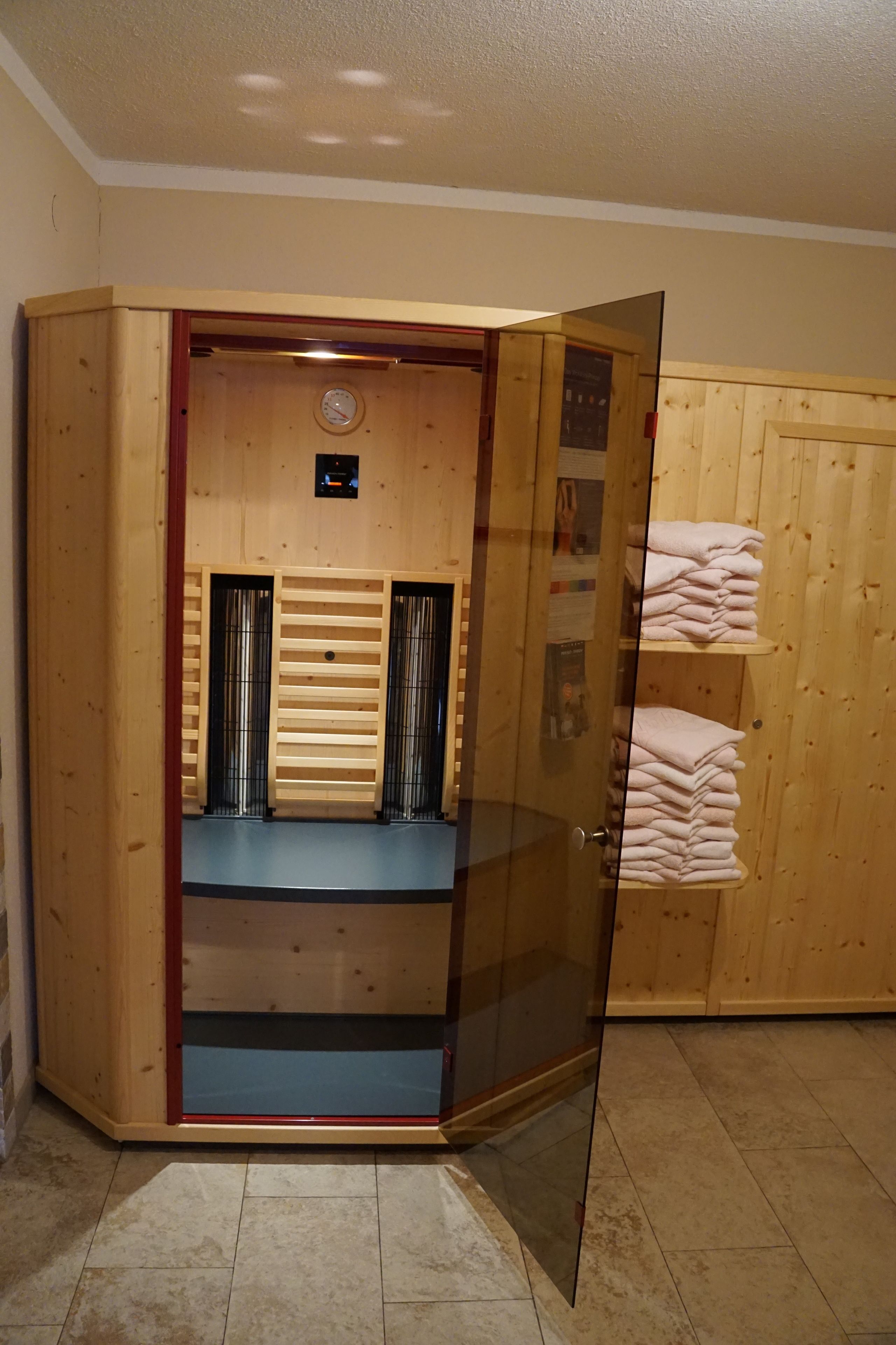 Een houten kast met een glazen deur, een klok en planken met opgevouwen handdoeken.