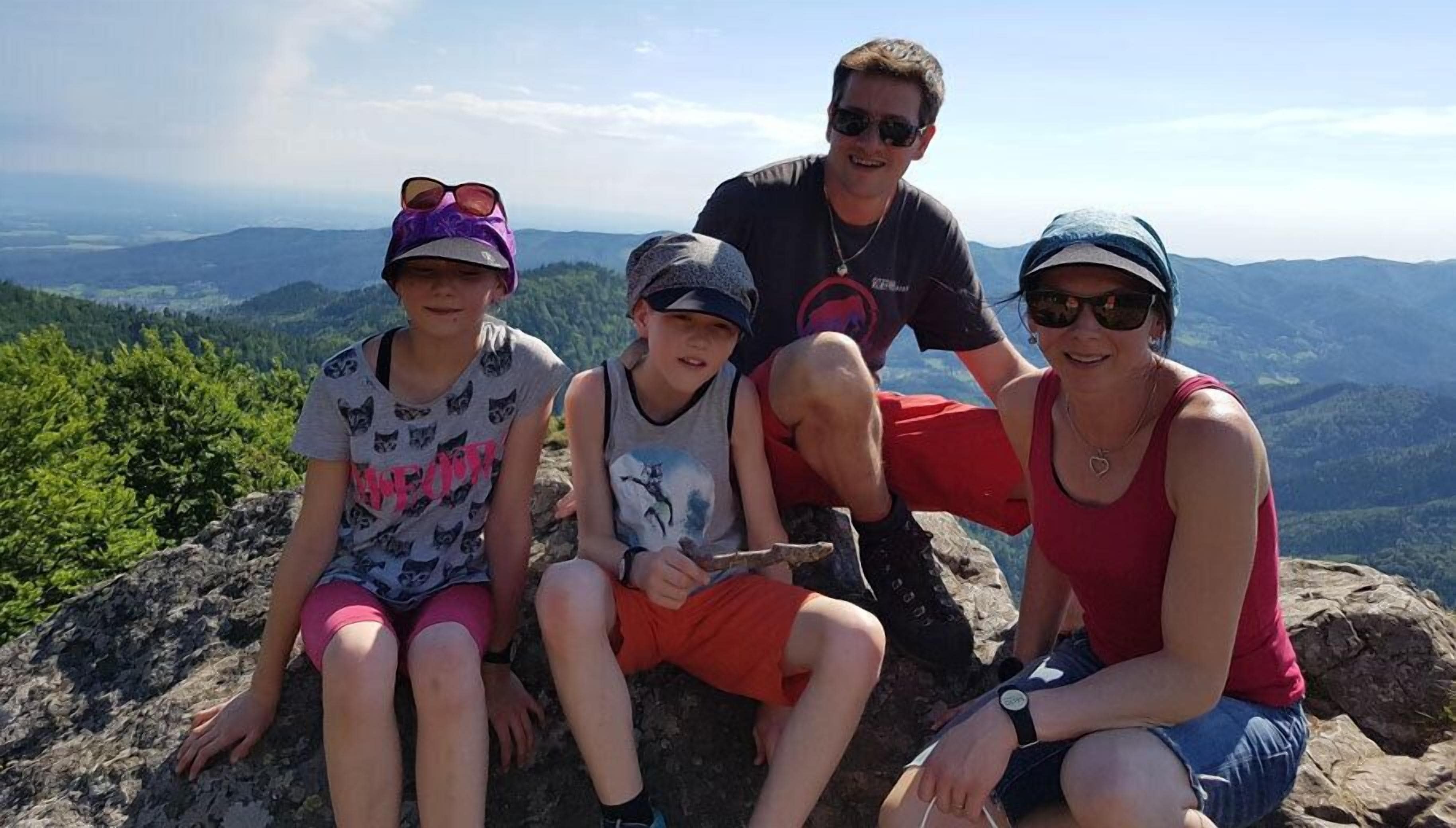 Eine vierköpfige Familie sitzt auf einem Felsen vor einer Berglandschaft.