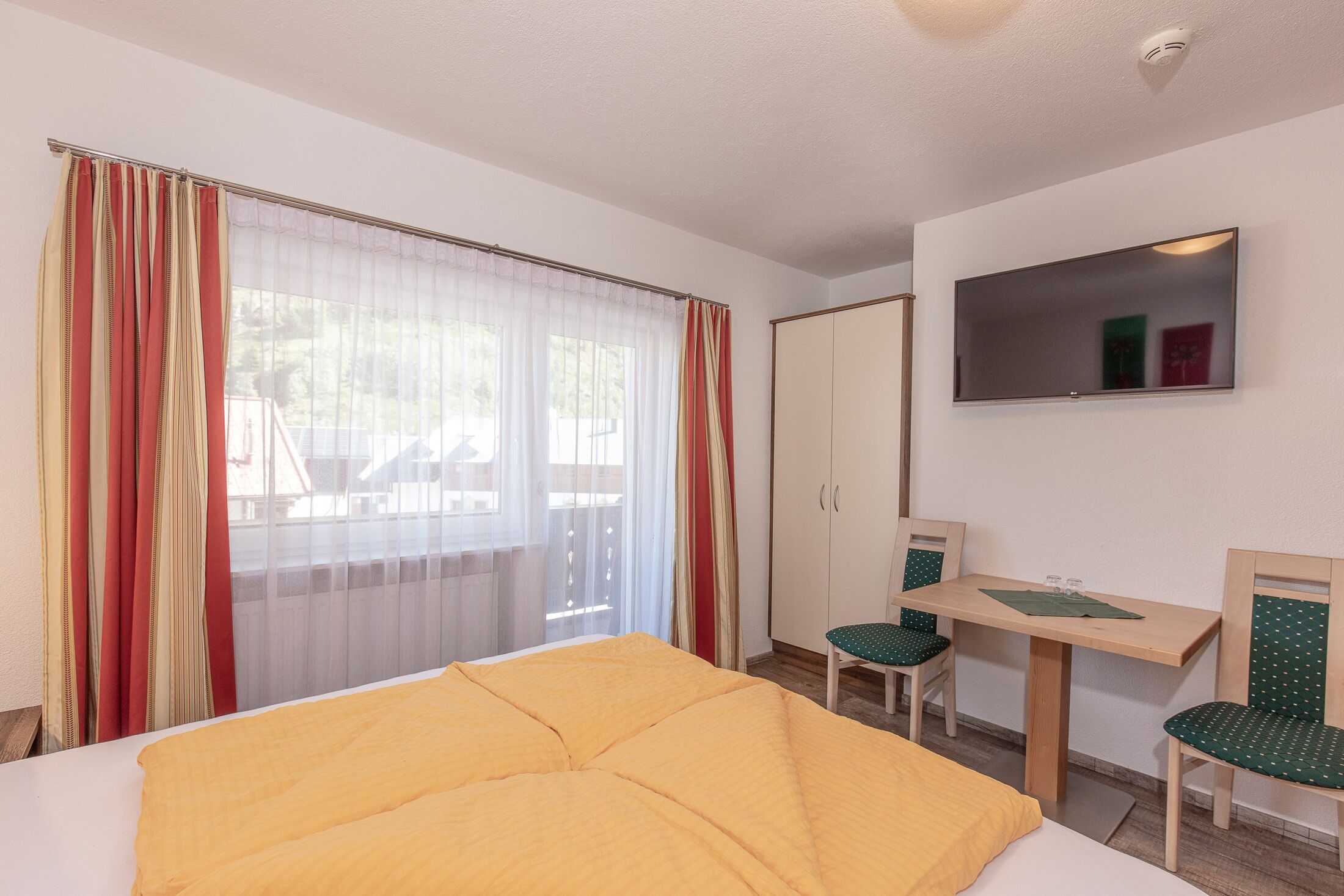 Una habitación de hotel con cama, escritorio, dos sillas, espejo y armario.