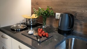 A kitchen counter with a stove, a kettle, a cutting board with tomatoes, a knife, and a vase with green leaves. - Apart Felsenhof (Laengenfeld)