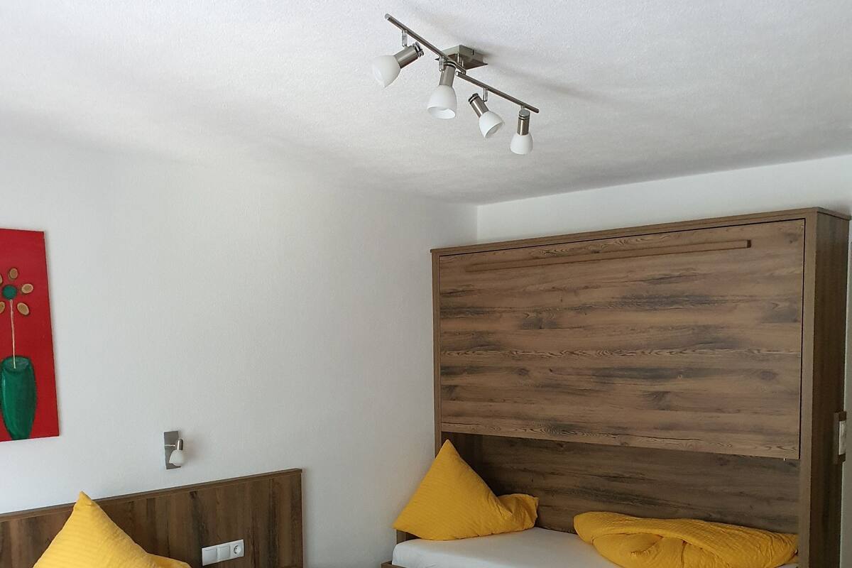 A room with two beds, each with a wooden headboard and yellow bedding. There is a ceiling light fixture above the beds.