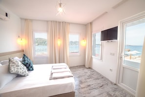 A hotel room with a bed, curtains, a television, and a view of the sea. - Madda Hotel (Bodrum)
