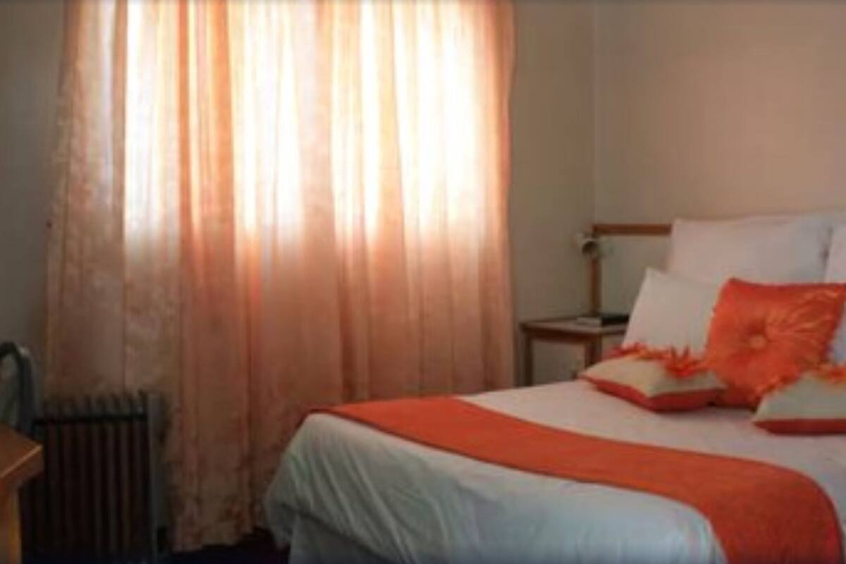 Una habitación de hotel con cama, mesita de noche y ventana con cortinas.