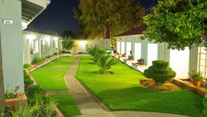 Un patio bien iluminado con césped cuidado, plantas en macetas y un sendero que lleva a un edificio.
