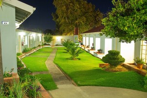 Un patio bien iluminado con césped cuidado, plantas en macetas y un sendero que lleva a un edificio.