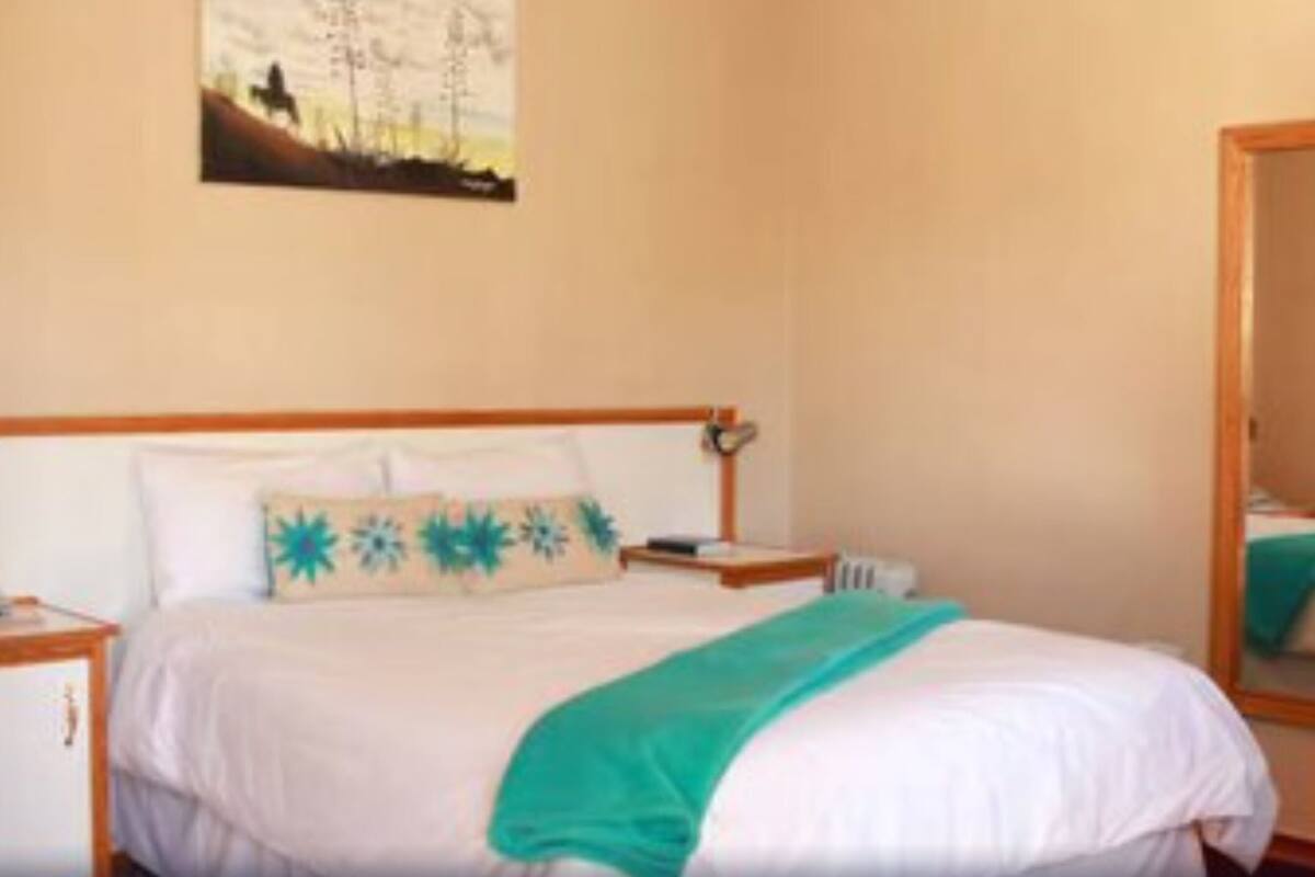 Un dormitorio con cama, mesita de noche, espejo y un cuadro en la pared.