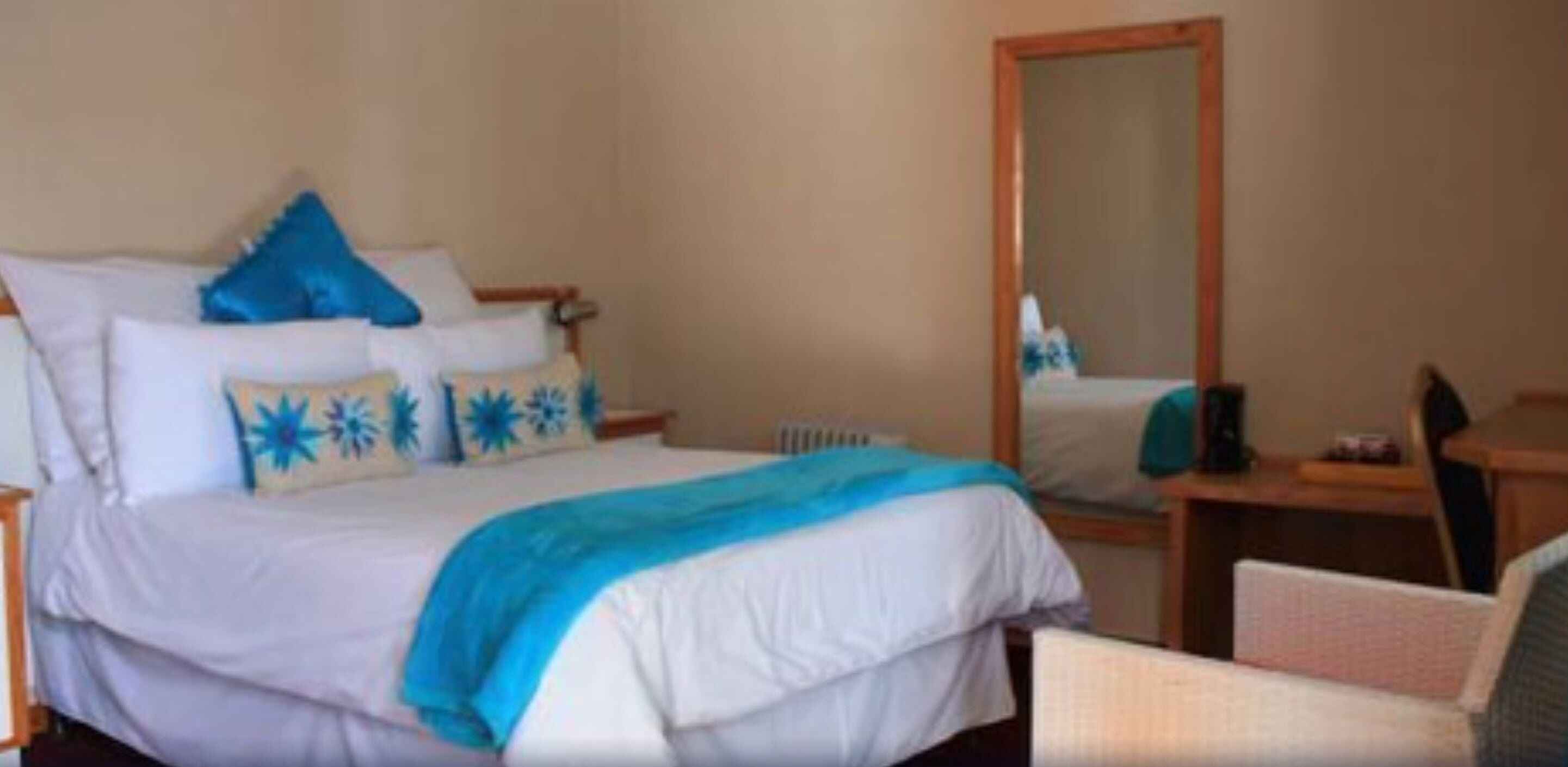 A hotel room with a bed, a chair, a desk, and a mirror.