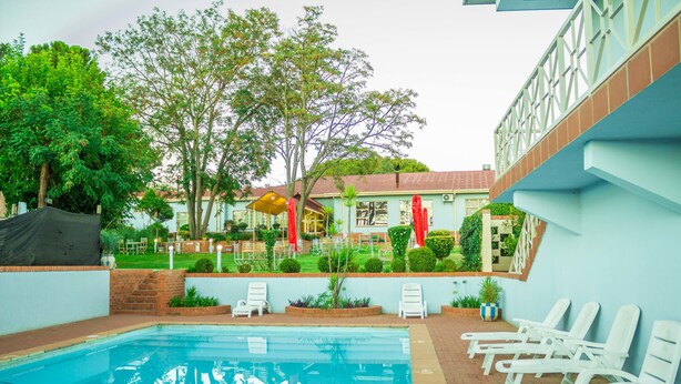 Una piscina con sillas de descanso, un área de patio techada y un edificio de fachada azul claro.