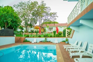 Una piscina con sillas de descanso, un área de patio techada y un edificio de fachada azul claro.