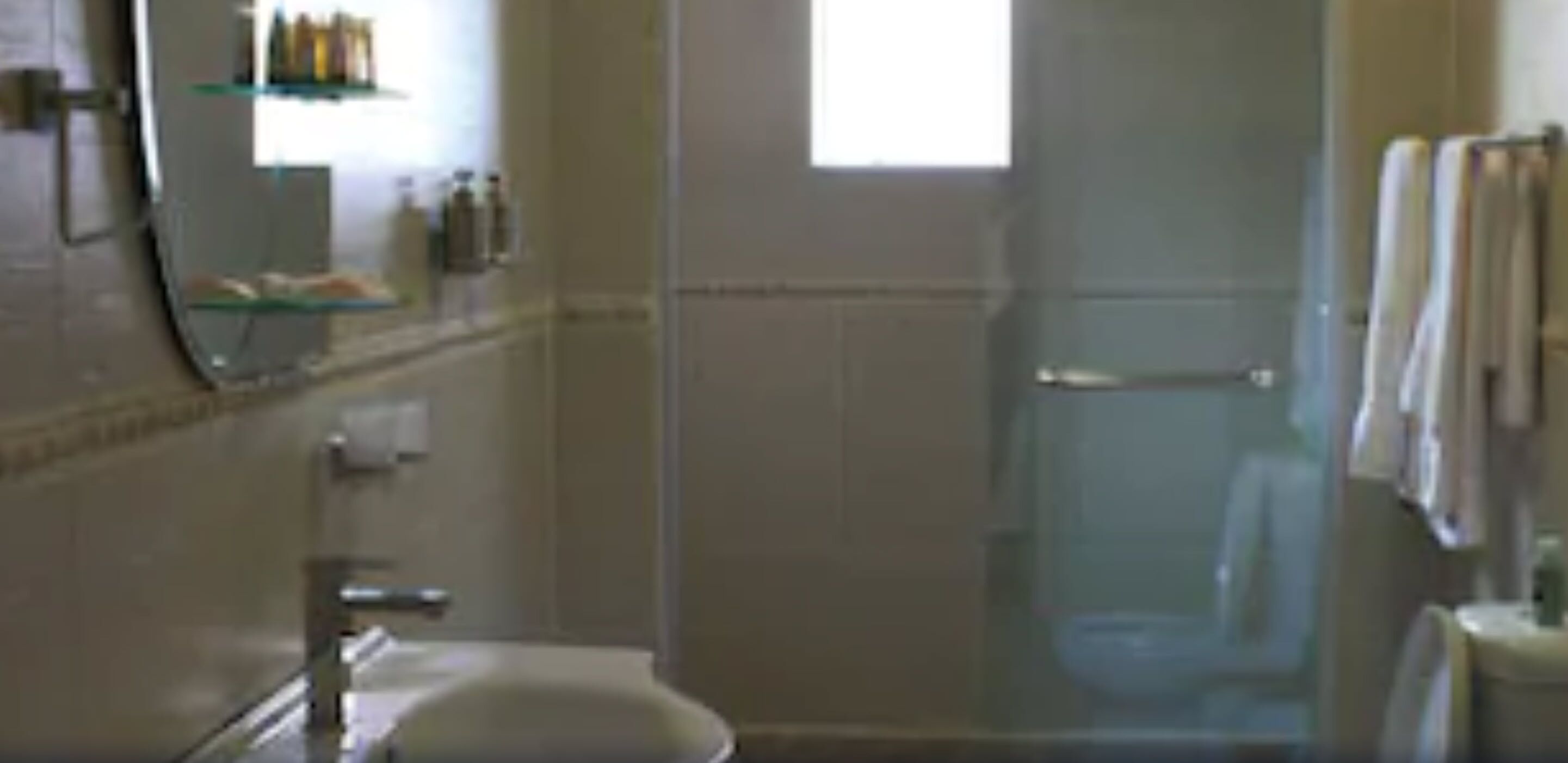 A bathroom with a glass shower enclosure, a sink, and a mirror.