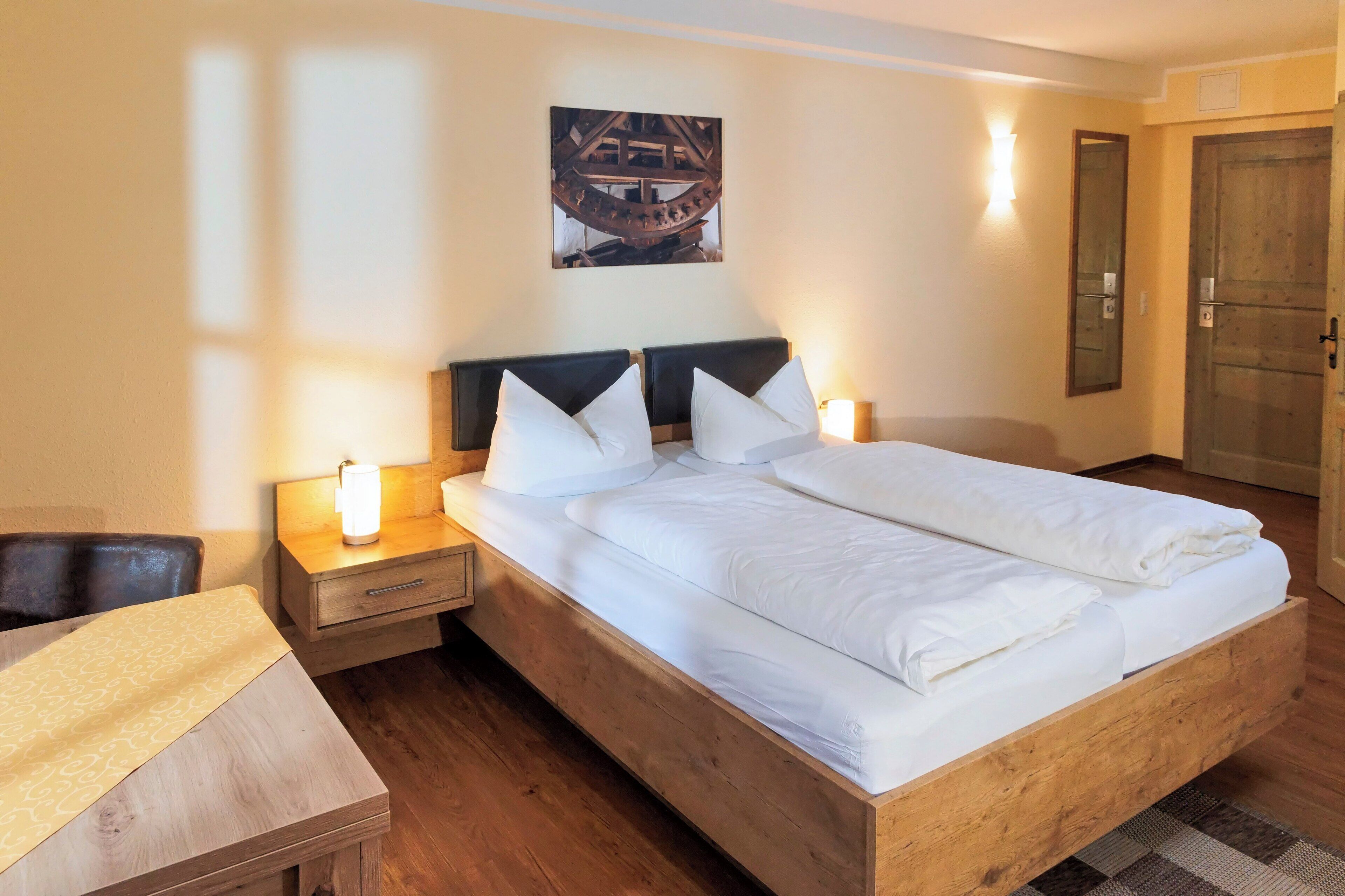 Ein ordentlich bezogenes Bett mit weißen Laken, einem Holzkopfende und zwei Nachttischen mit Lampen.
