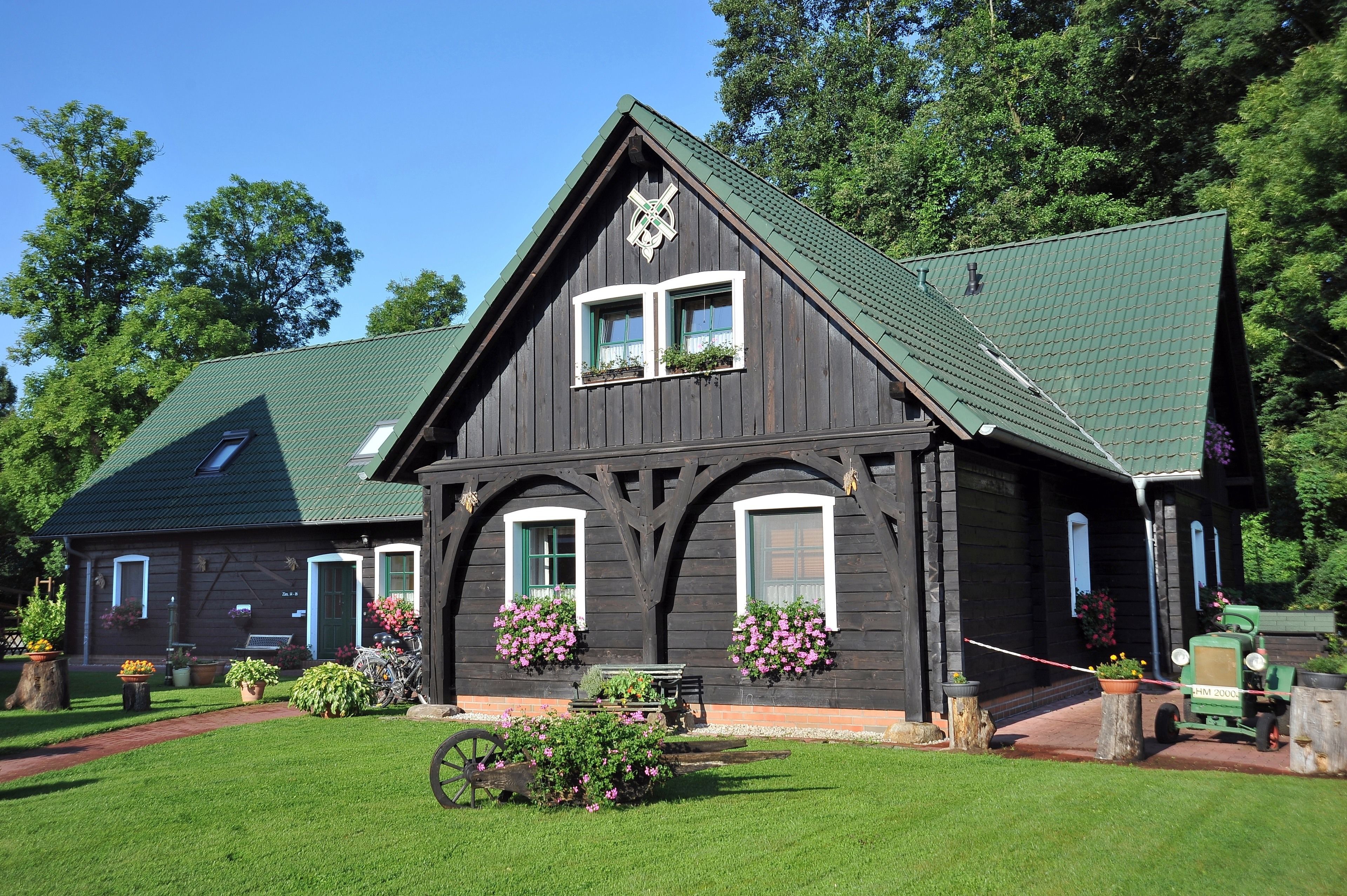 A traditional wooden building with a steep gable roof, two windows with green shutters, and flower boxes on the front.