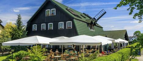 A large black building with a windmill, outdoor seating, and a garden.