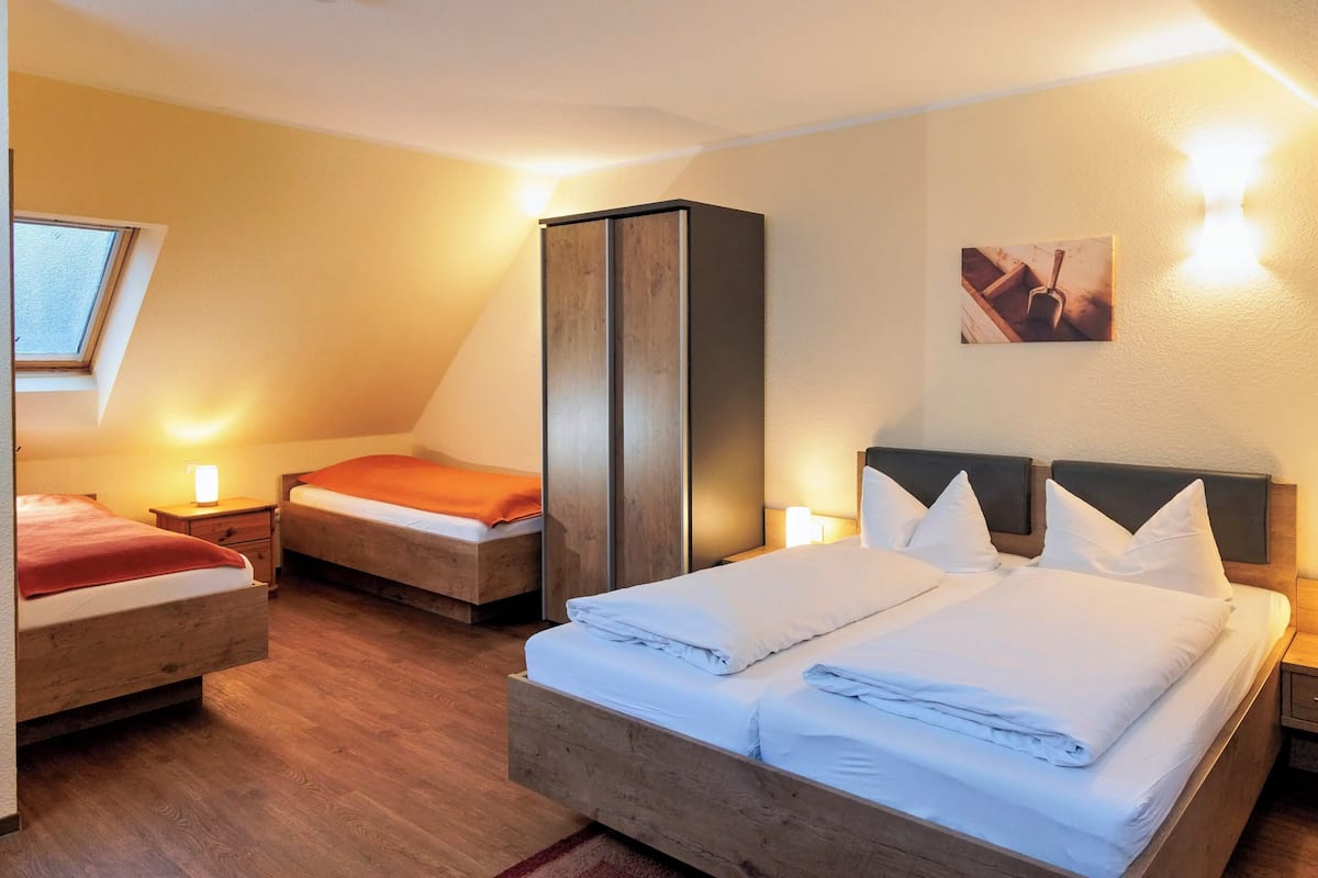 A hotel room with two beds, a wardrobe, a small table, and a wall-mounted lamp.