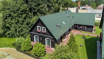 A large, two-story building with a green roof, surrounded by lush greenery and a well-maintained lawn.