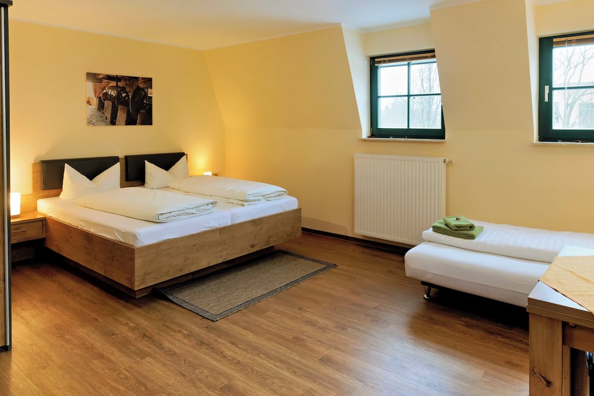 A bedroom with a wooden bed, a smaller sofa, a radiator, and a window.