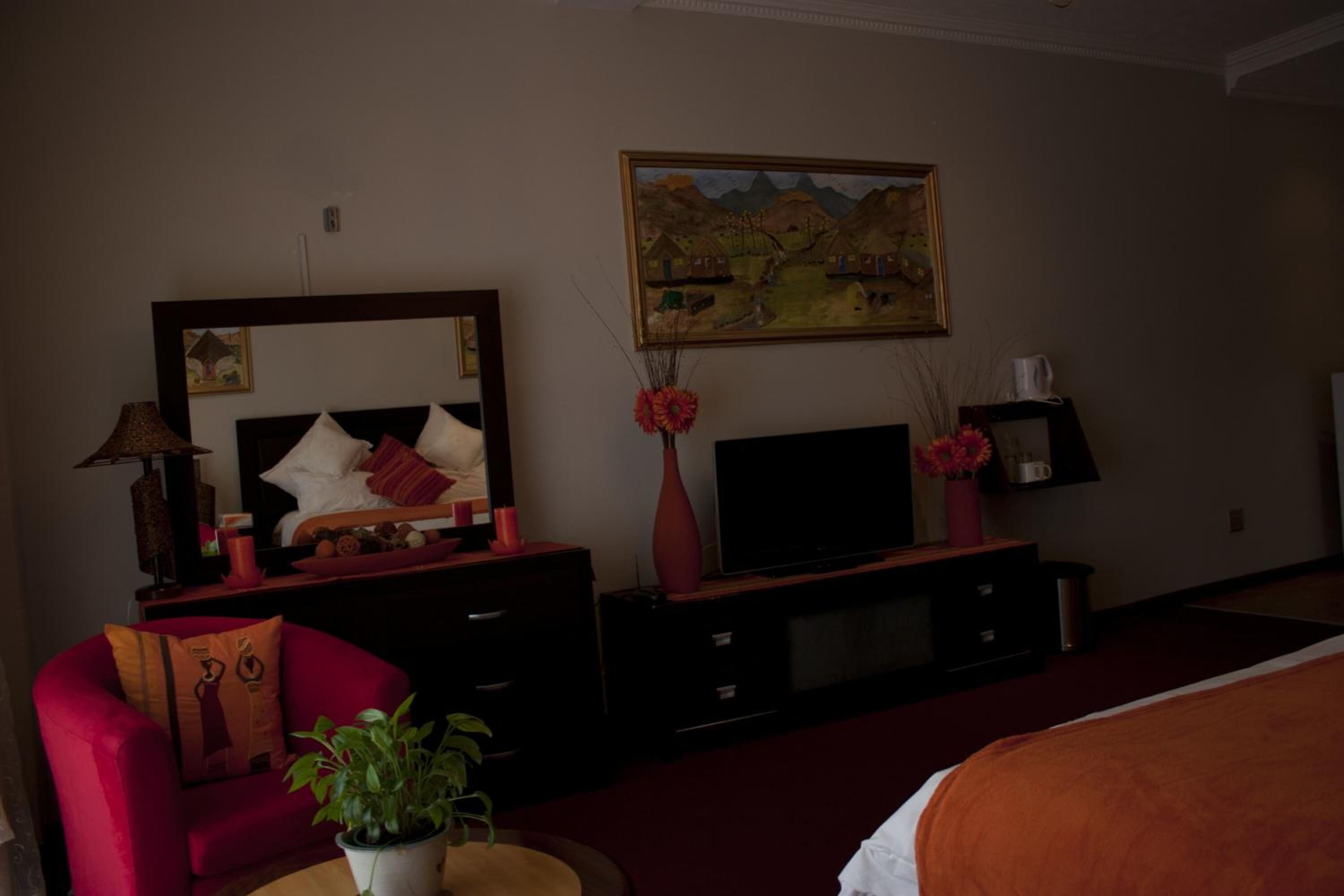 A hotel room with a bed, a TV, a red armchair, a dresser, a mirror, and a painting on the wall.