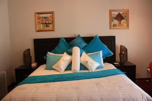 Una cama bien hecha con ropa de cama azul y blanca, dos mesitas de noche con adornos, y dos cuadros en la pared.